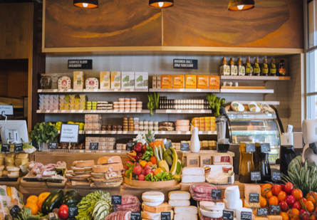 The image captures a sophisticated yet cozy high-end grocery store in Austin, TX, showcasing a vibrant array of premium, locally sourced goods including fresh produce, artisanal meats, seafood, dairy, cheeses, and pantry staples, with an inviting artisanal deli offering sandwiches, salads, pastries, and coffee, all set in a warm atmosphere that subtly hints at online ordering and delivery, reflecting the community-focused and mindful indulgence ethos appealing to modern, health-conscious urban dwellers in the South Congress and Hyde Park areas.